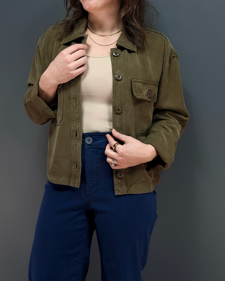 Woman wearing green button up utility style jacket with navy wide leg pants in front of a gray background