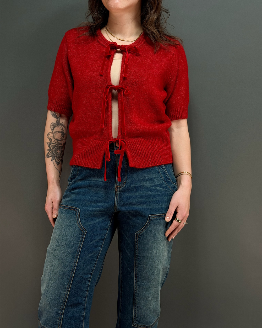 woman wearing red tie front cardigan with jeans in front of a gray background