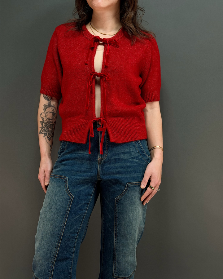 woman wearing red tie front cardigan with jeans in front of a gray background