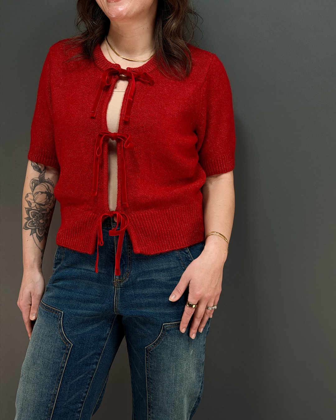 woman wearing red tie front cardigan with jeans in front of a gray background