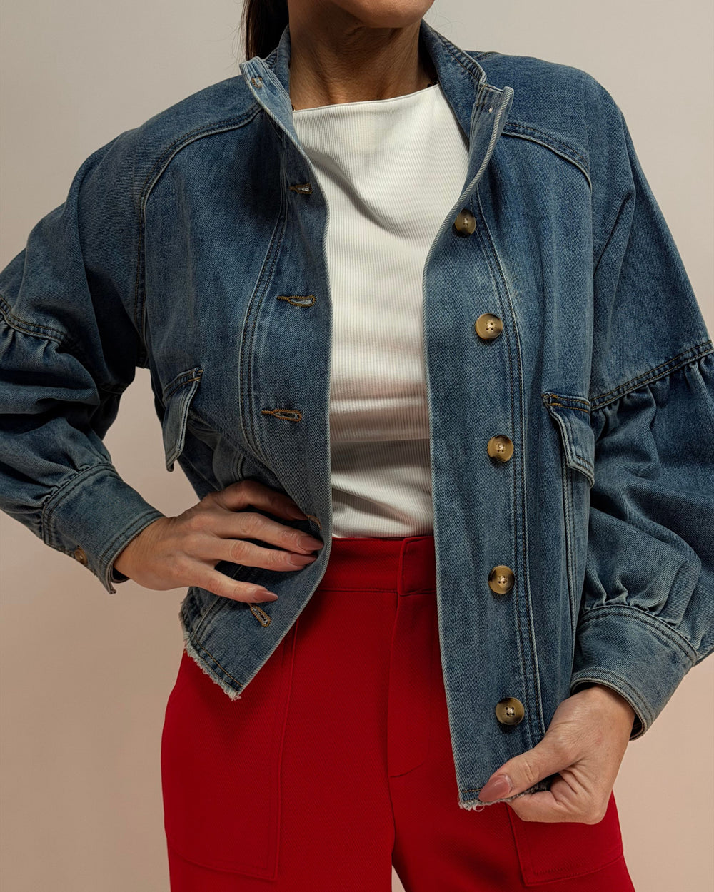 Person wearing a blue denim jacket over a white shirt and red pants on a beige background