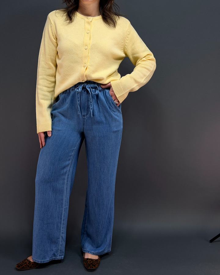woman wearing a yellow cardigan with blue wide leg tie waist pants in front of a gray background