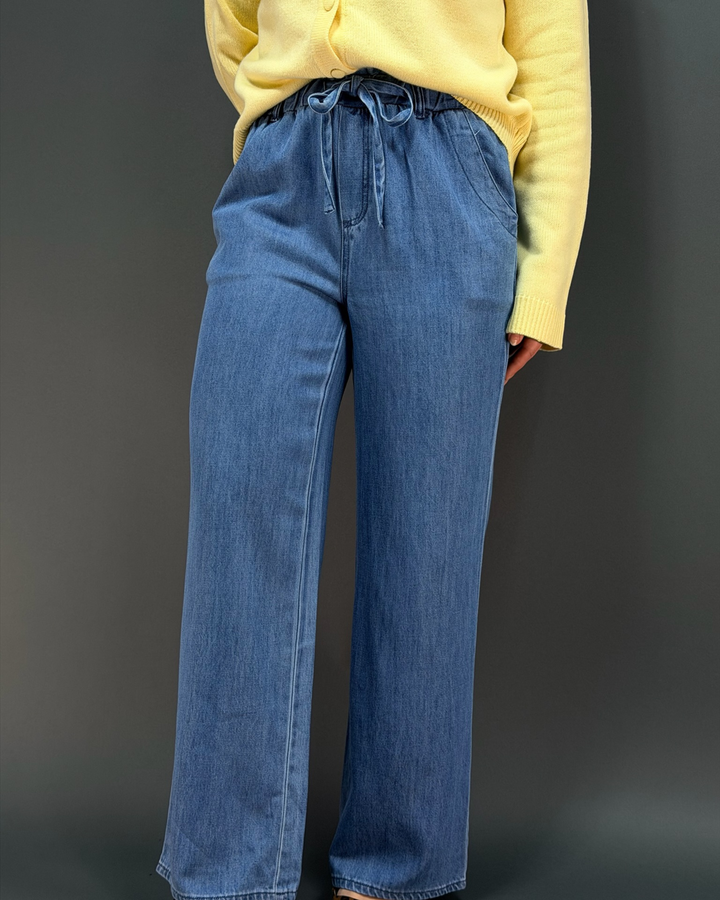 woman wearing a yellow cardigan with blue wide leg tie waist pants in front of a gray background