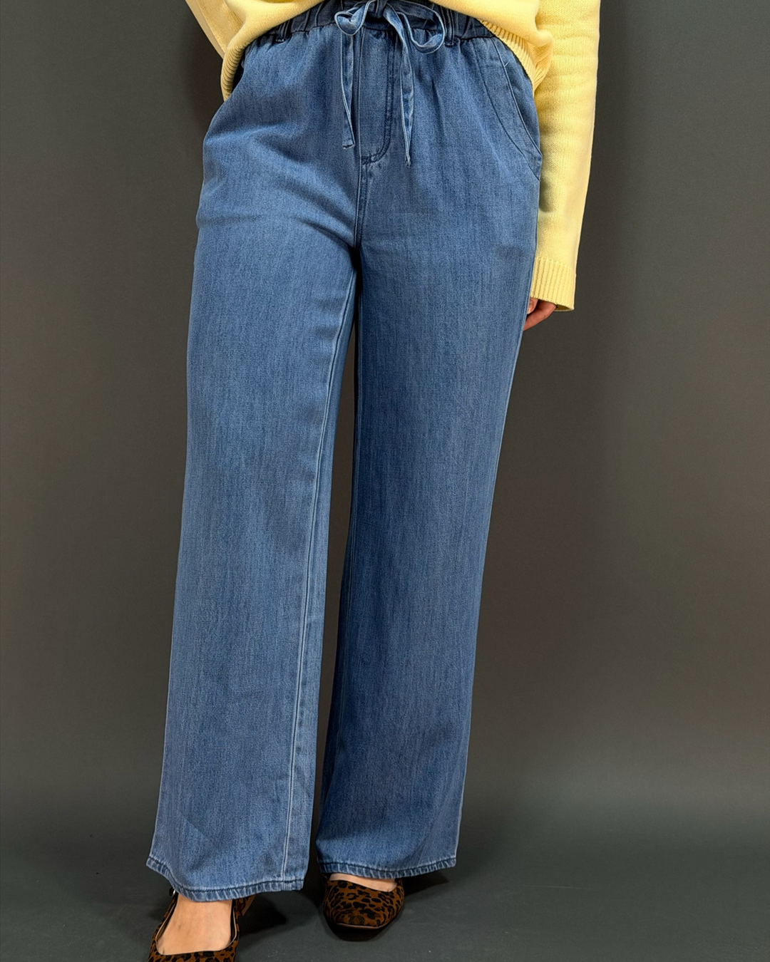 woman wearing a yellow cardigan with blue wide leg tie waist pants in front of a gray background
