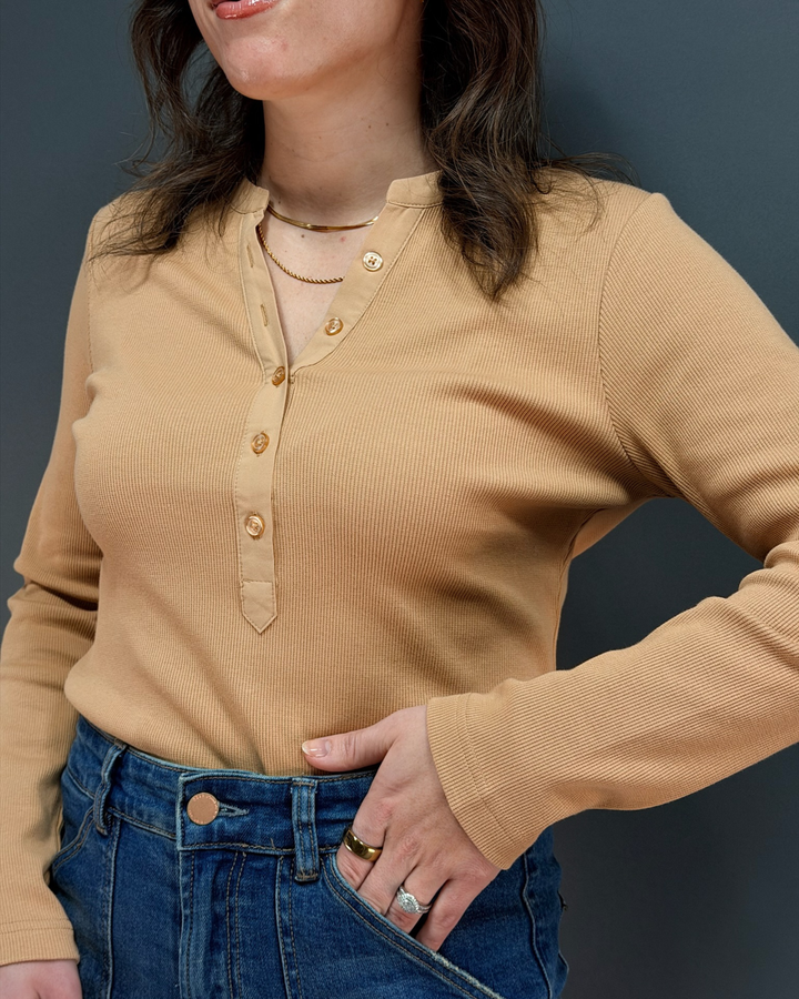 woman wearing tan long sleeve top with jeans in front of gray background