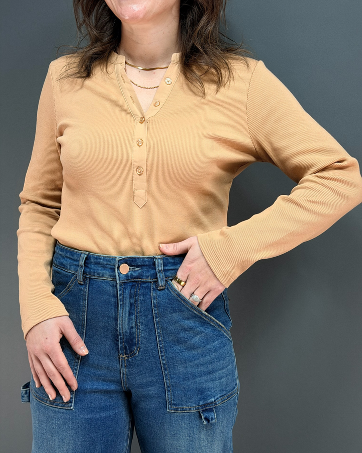 woman wearing tan long sleeve top with jeans in front of gray background