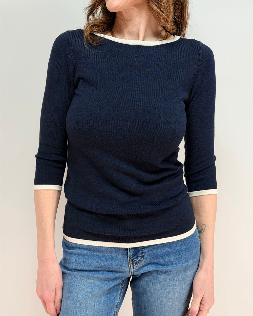 Person wearing a navy blue sweater with white trim and blue jeans on a plain background
