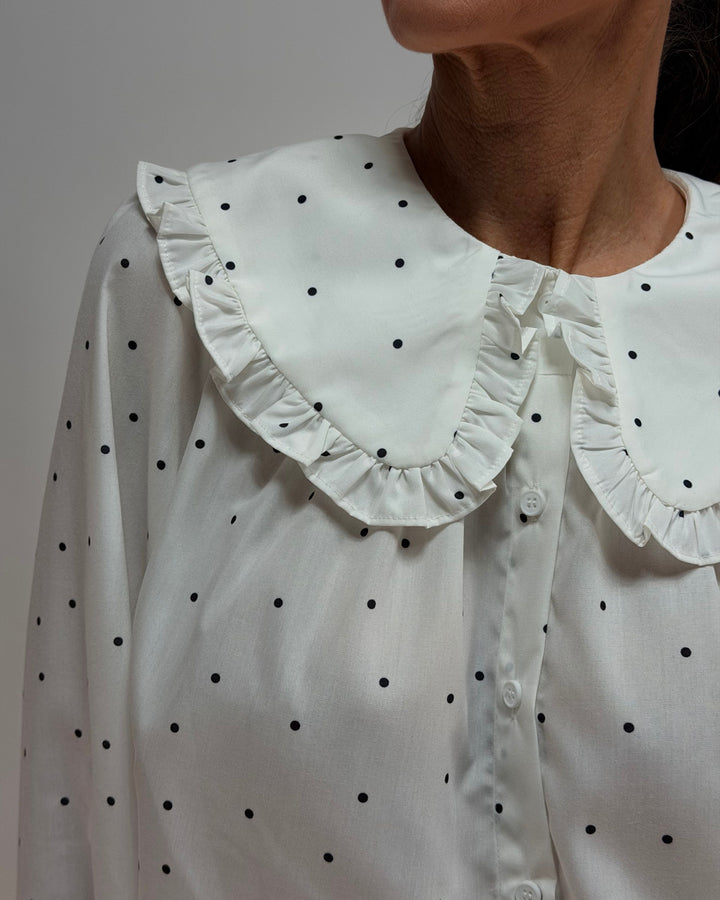White blouse with black polka dots and ruffled collar on a plain background