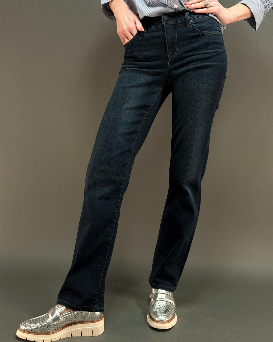 woman wearing dark wash jeans in front of a gray background