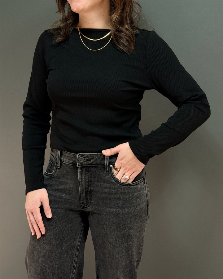 woman wearing long sleeve black top with charcoal colored jeans in front of gray background