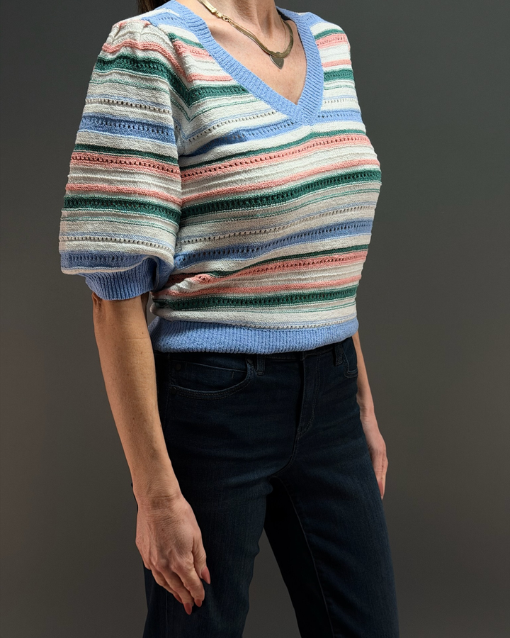 woman wearing a short colorful striped knit sweater with dark wash jeans in front of a gray background