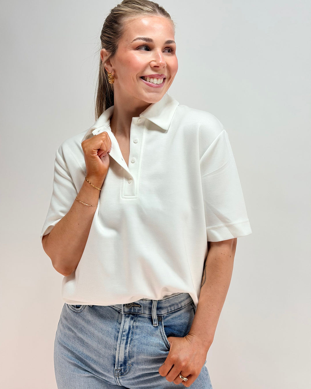 Woman wearing a white polo shirt and blue jeans against a plain background