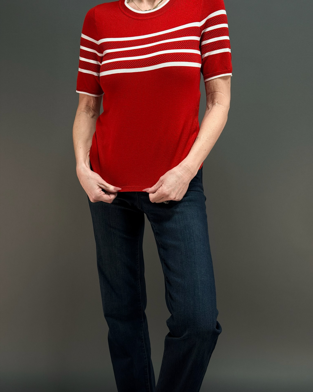 woman wearing a short sleeve red sweater with white stripes, with dark wash jeans in front of a gray background