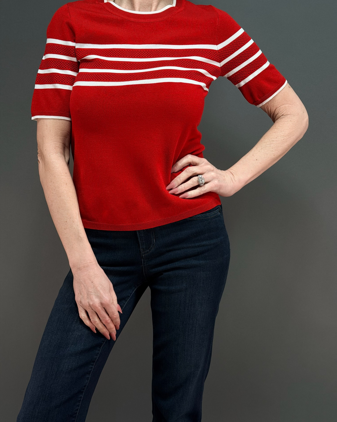 woman wearing a short sleeve red sweater with white stripes, with dark wash jeans in front of a gray background