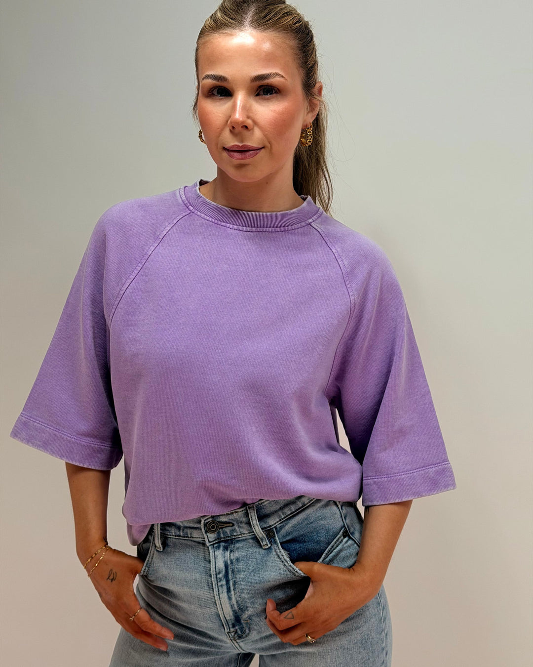 Woman wearing a purple oversized shirt and blue jeans against a plain background