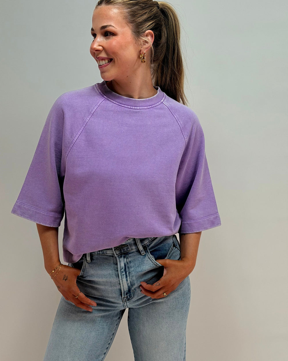 Woman wearing a purple oversized shirt and blue jeans against a plain background
