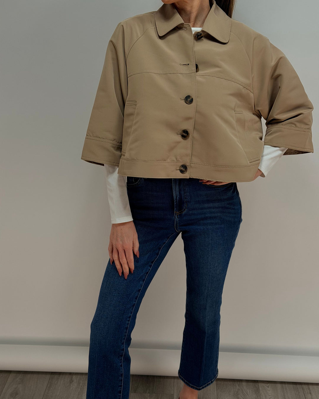 Person wearing a beige jacket and blue jeans against a plain background