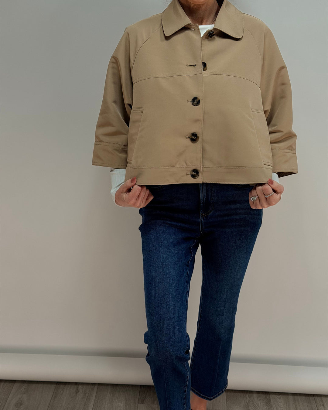 Person wearing a beige jacket and blue jeans against a plain background