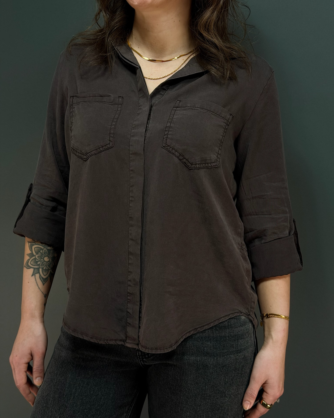 woman wearing a cool tone brown button down top with black jeans in front of a gray background