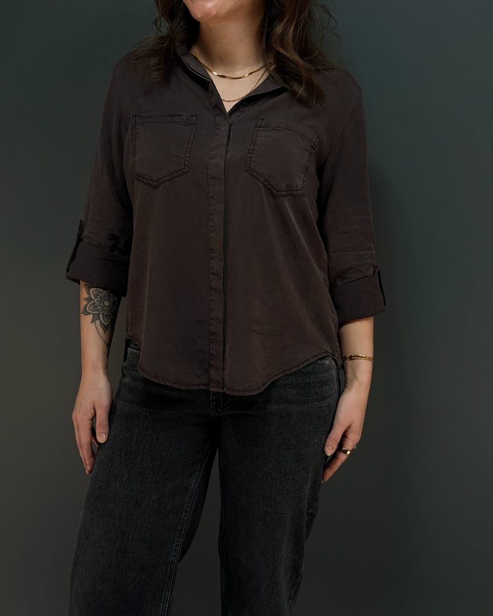 woman wearing a cool tone brown button down top with black jeans in front of a gray background