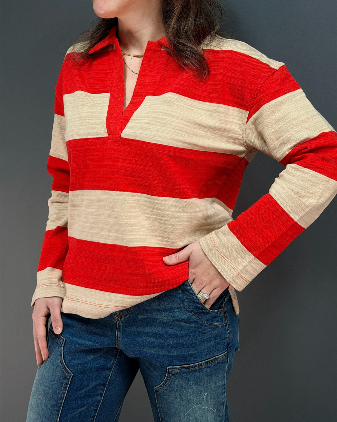 woman wearing red and tan striped rugby top with jeans in front of a gray background