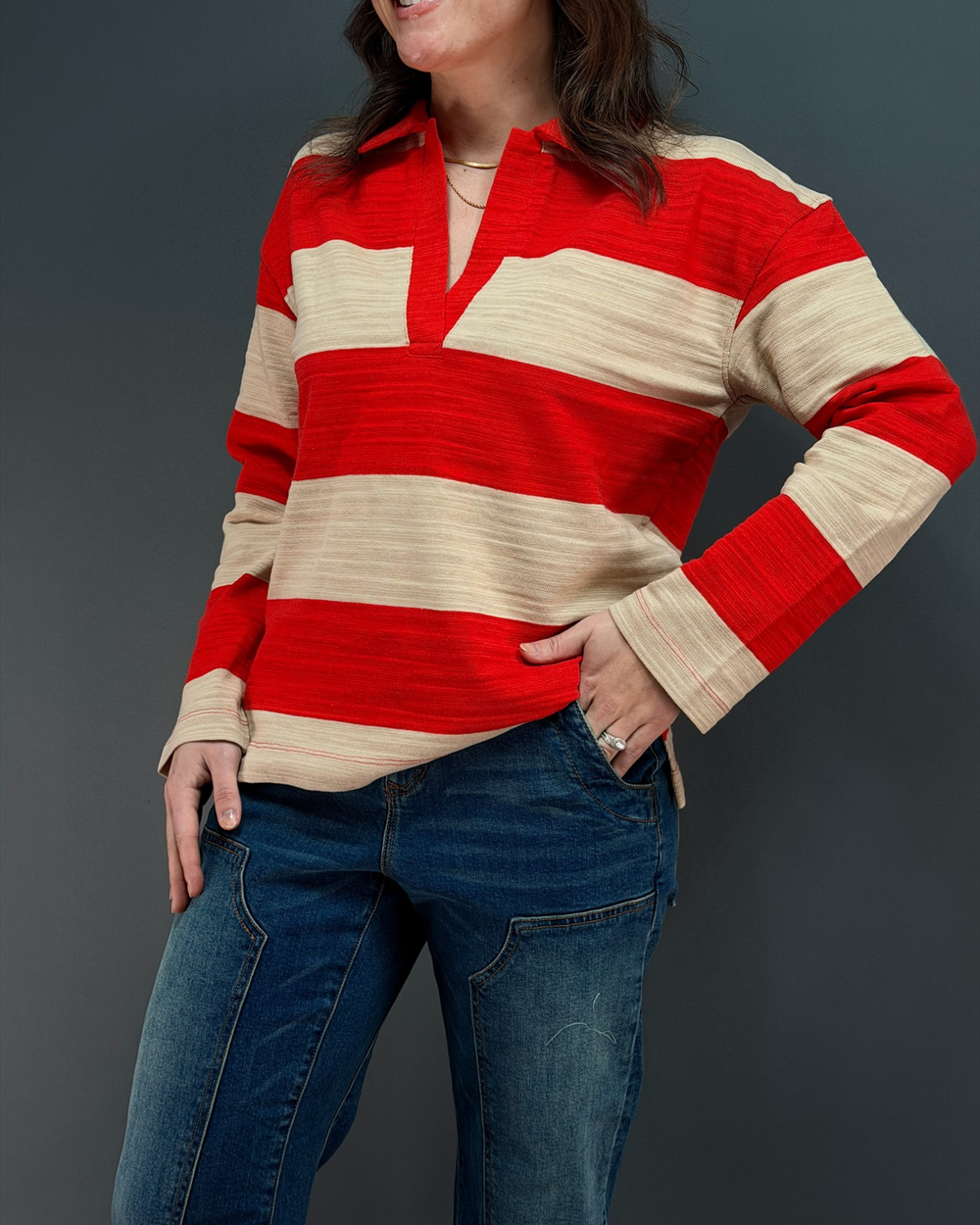 woman wearing red and tan striped rugby top with jeans in front of a gray background