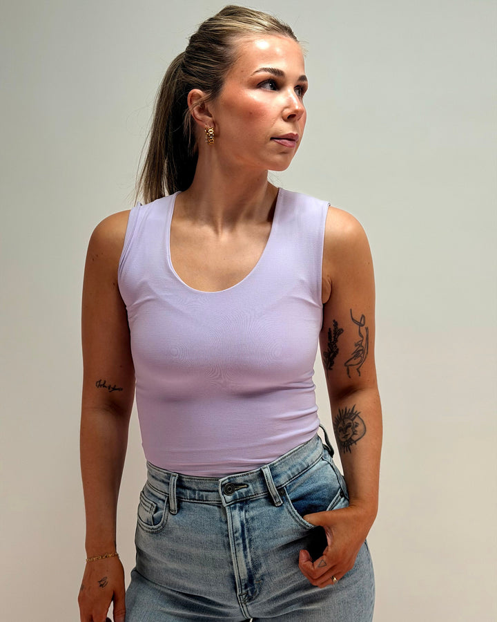 woman wearing purple tank top and blue jeans in front of a plain background