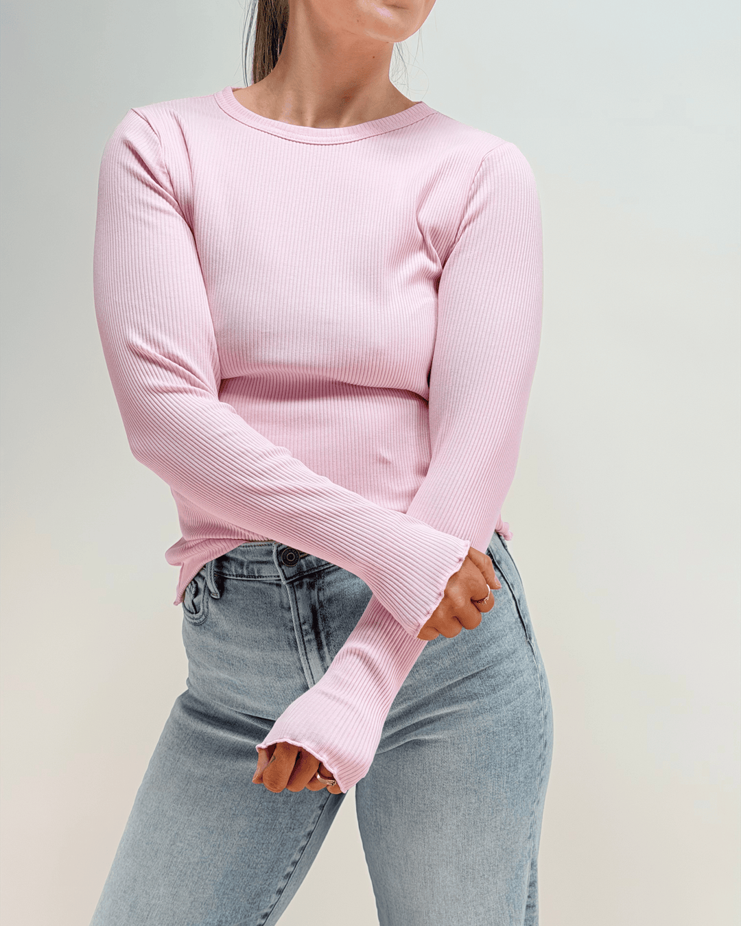 Person wearing a pink ribbed sweater and light blue jeans against a plain background