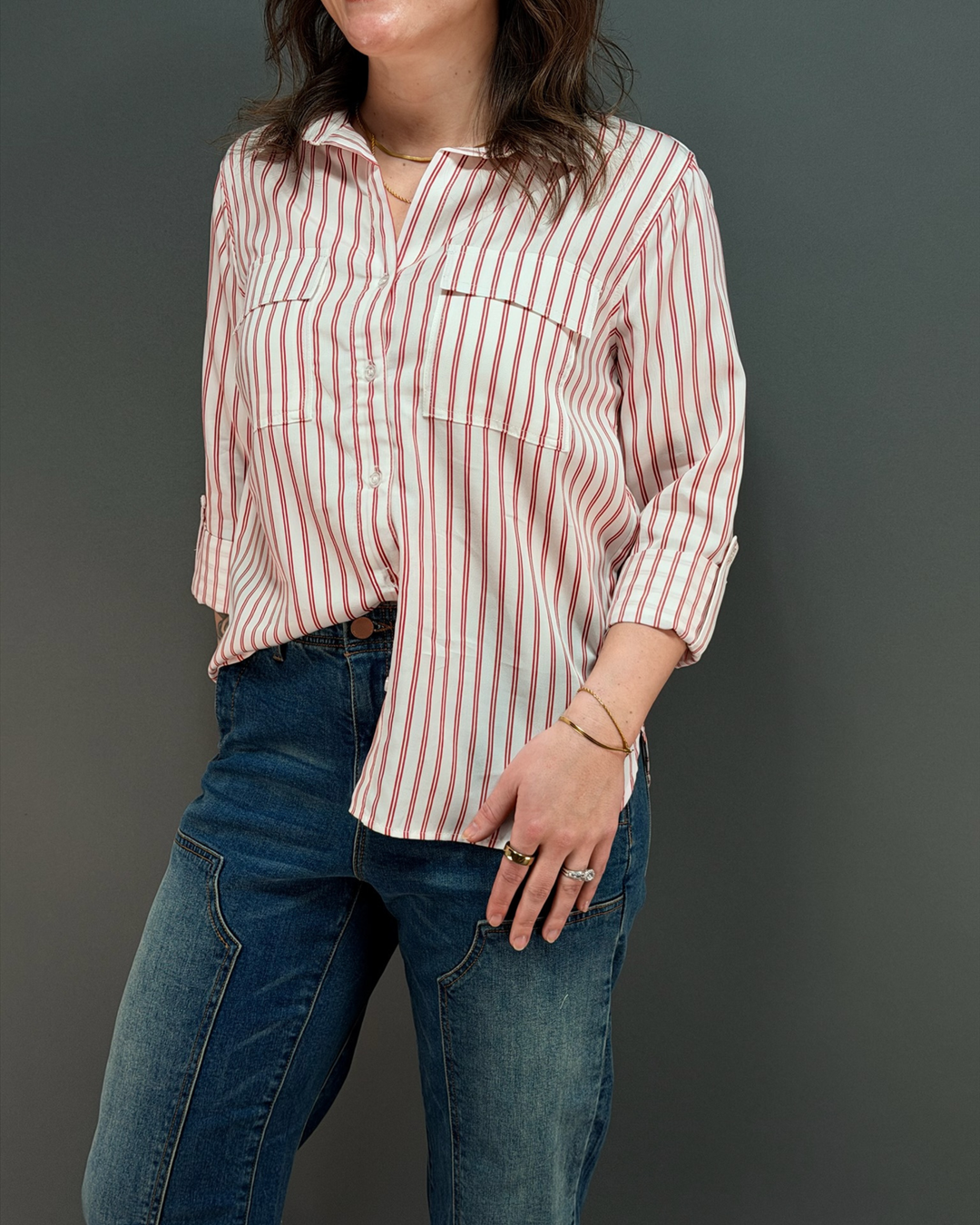 woman wearing a red and white striped button down top with jeans in front of a gray background