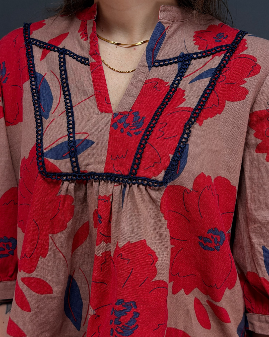 woman wearing tan and red floral blouse with navy pants in front of a gray background