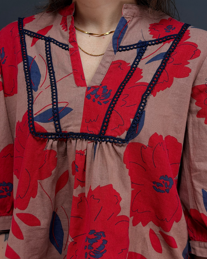 woman wearing tan and red floral blouse with navy pants in front of a gray background